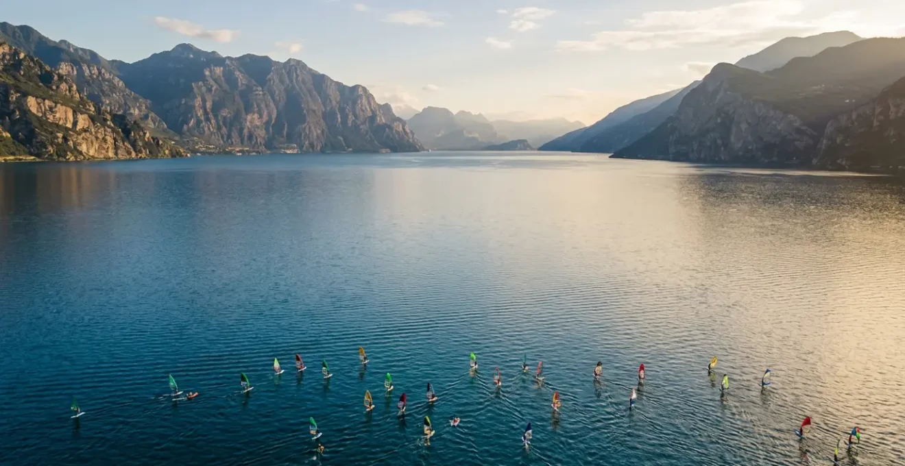 Vista aerea del Lago di Garda con vele colorate di windsurf e kitesurf sull'acqua blu con montagne sullo sfondo
