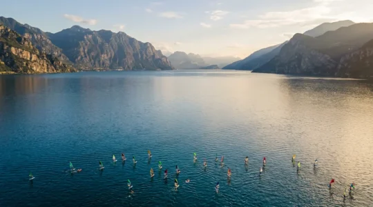 Vista aerea del Lago di Garda con vele colorate di windsurf e kitesurf sull'acqua blu con montagne sullo sfondo