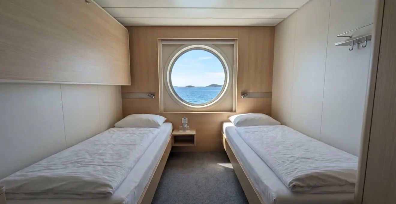 Interno di una cabina moderna di traghetto con letti preparati e oblò che mostra il mare