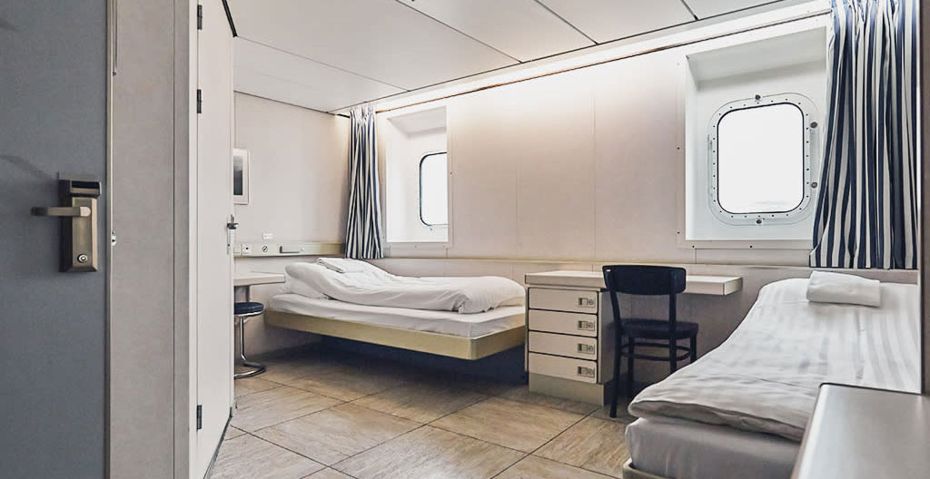Interno di una cabina traghetto moderna per 4 persone vuota e ordinata con letti, oblò e luce naturale Interno di una cabina traghetto moderna per 4 persone vuota e ordinata con letti, oblò e luce naturale